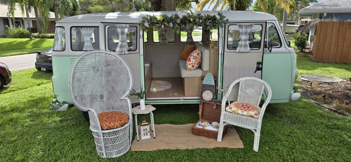 Darla the VW bus set up on the lawn with wicker chairs, a woven rug, and a picnic basket